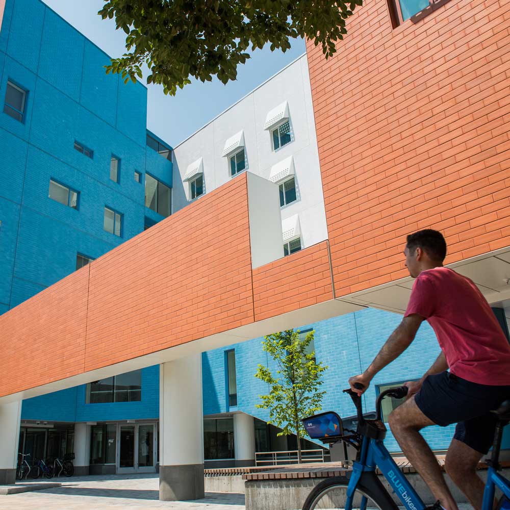 Image of the front of the Vassar Street dorm with a bicyclist passing by.